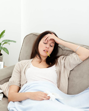 生病的女人在家里的沙發(fā)上用體溫計(jì)量體溫