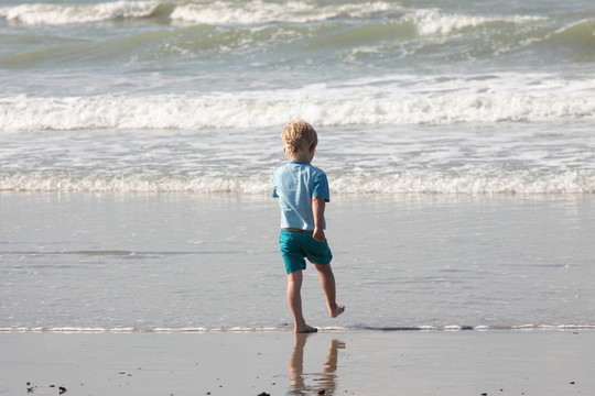 年幼的孩子走在沙灘上的波浪
