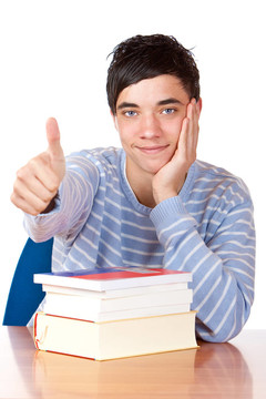 年轻快乐的学生坐在书桌上，拿着书，竖起大拇指