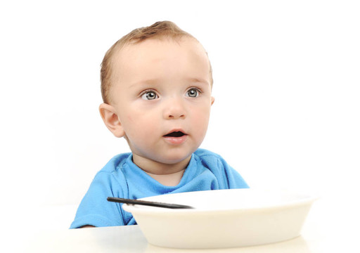 可愛的可愛的一歲的嬰兒在桌子上吃綠色的眼睛；勺子和盤子