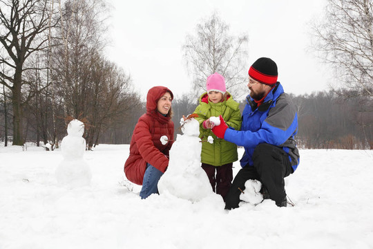 從三人的家庭在公園在冬季和雕塑的雪人