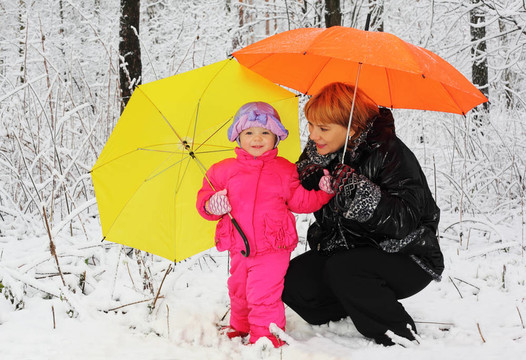 祖母和孫女帶著黃色和橙色的雨傘站在冬天的雪地里