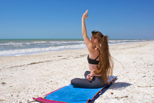 女子做瑜伽练习在海滩上绑定半莲花姿势或