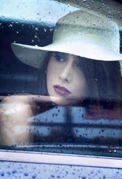 年輕迷人的女人透過窗戶看雨后