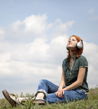 年轻的姑娘微笑着耳机坐在绿色的草。