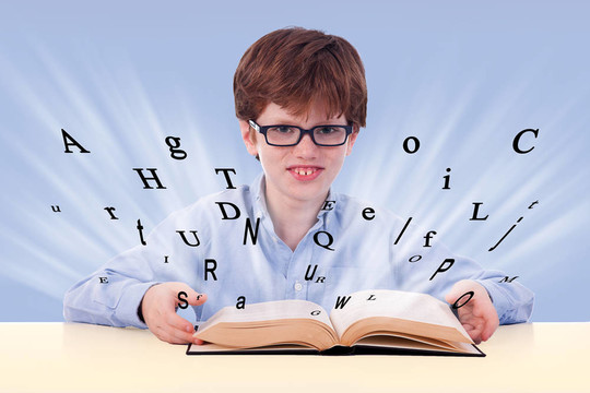 可愛的男孩在桌子上讀著一本書；帶著字母；藍色的孤立；工作室的鏡頭