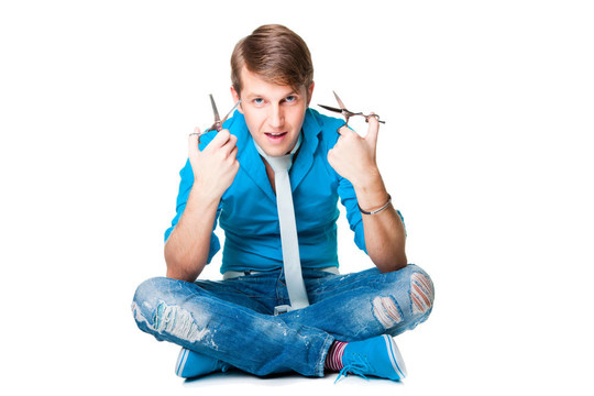 年輕漂亮的男理發(fā)師穿著藍(lán)色襯衫和白色領(lǐng)帶夾著兩個剪刀坐在白色背景上