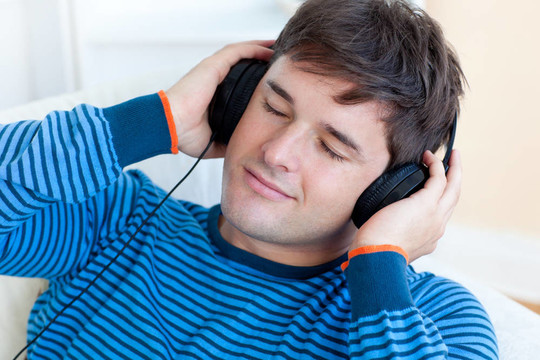 和平的人聽(tīng)音樂(lè)抱著他的earphoneslying在客廳沙發(fā)上