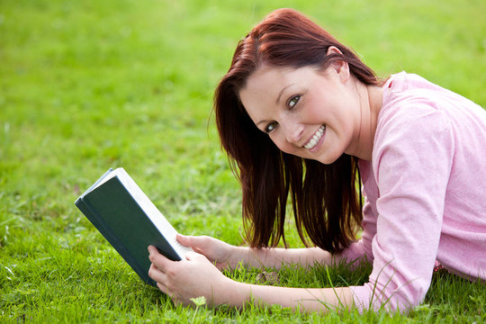 可愛的女人躺在草地上看書