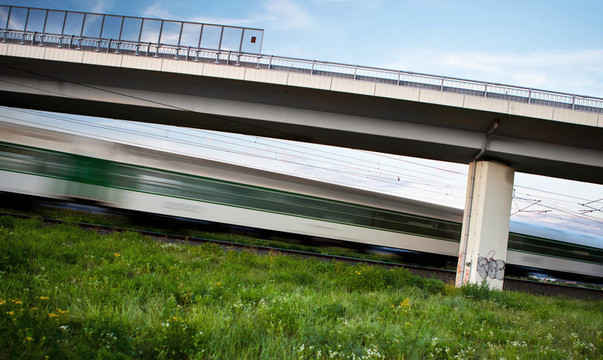 快速列車快速穿過夏季景觀，并通過公路橋