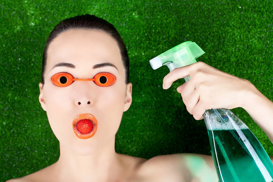 特寫鏡頭的一個(gè)美麗的女人帶著日光浴床的眼鏡與草莓的嘴和噴霧瓶在一方面對(duì)綠色