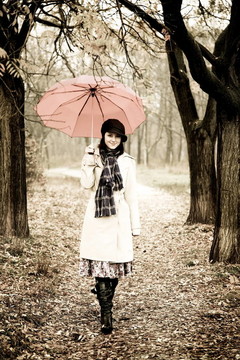 下雨天在公园里带着雨伞和围巾的女孩。照片与自然色彩的复古风格。