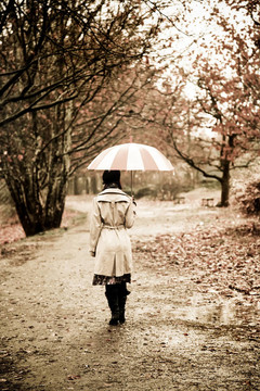 下雨天在公園里帶著雨傘和圍巾的女孩。照片與自然色彩的復(fù)古風格。