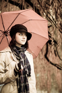 下雨天在公园里带着雨伞和围巾的女孩。照片与自然色彩的复古风格。