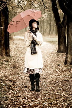 下雨天在公園里帶著雨傘和圍巾的女孩。照片與自然色彩的復(fù)古風(fēng)格。