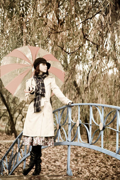 下雨天在公園里帶著雨傘和圍巾的女孩。照片與自然色彩的復(fù)古風(fēng)格。