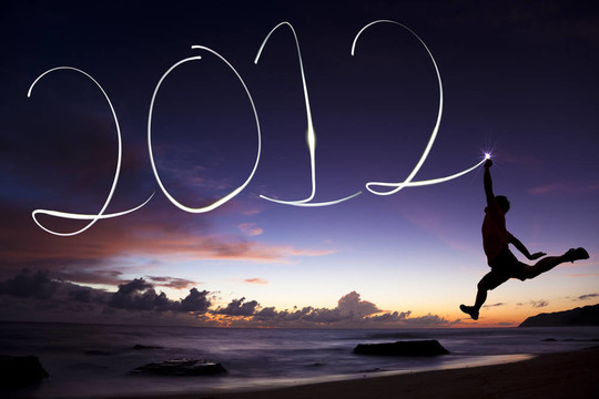 新年快樂(lè)2012。年輕人在日出前在海灘上用手電筒在空中跳躍和畫畫2012