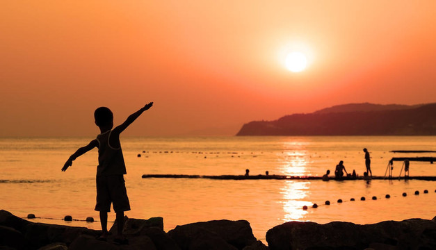孩子在海上曬橘色夕陽(yáng)的剪影，攤開(kāi)雙手