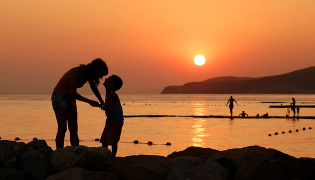 剪影的孩子和他的母親在橙色的夕陽(yáng)在海上