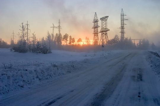 一條冰雪覆蓋的道路環(huán)繞著森林，電線傳送和日落的背景