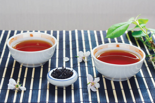 兩杯茶；盛滿茶葉的葉子和櫻桃，還有竹葉上的靜物桌布
