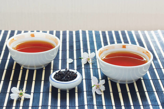 兩杯茶；一罐茶葉和櫻花在竹桌布上靜物