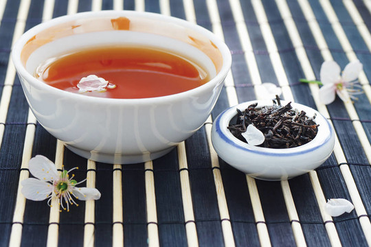 一杯茶；茶葉罐和櫻花在竹子桌布上依然存在