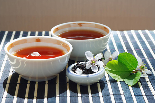 兩杯茶；盛滿茶葉的葉子和櫻桃，還有竹葉上的靜物桌布