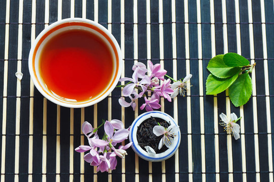 一杯茶；一罐茶葉和櫻花，還有丁香葉在竹臺(tái)布上的靜物