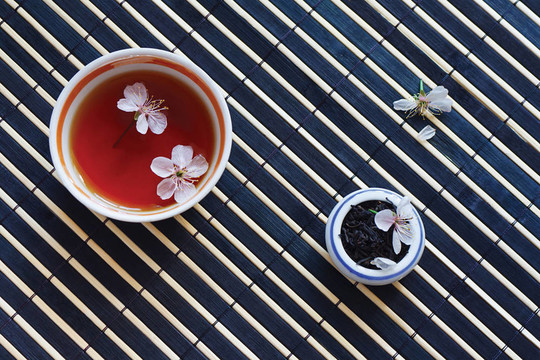 一杯茶；茶葉罐和櫻花在竹子桌布上依然存在