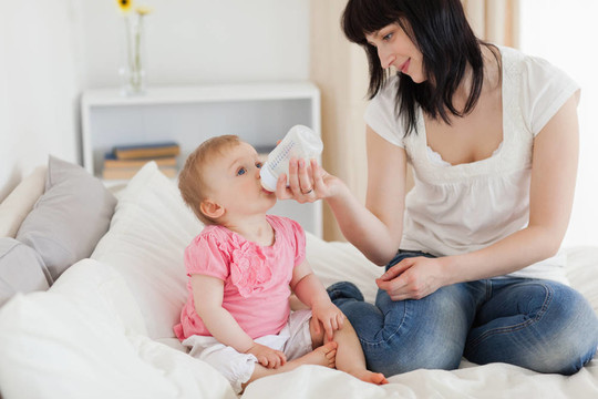 迷人的黑發(fā)女瓶喂她的嬰兒床上