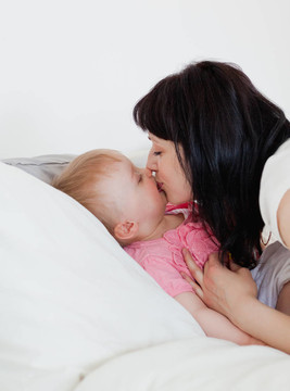 可愛的黑發(fā)女人給一個(gè)吻，她的嬰兒在床上
