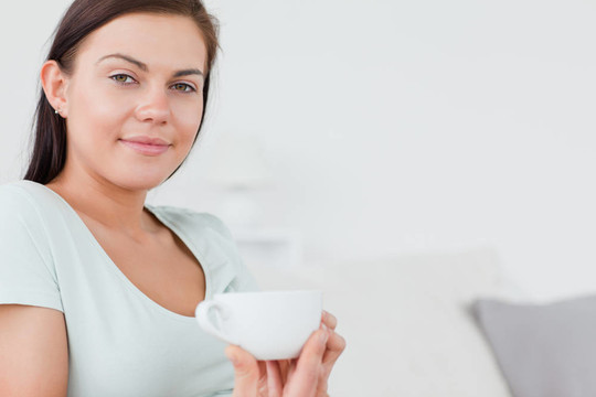 一個(gè)迷人的女人坐在沙發(fā)上喝著一杯茶看著相機(jī)