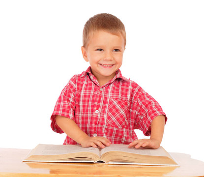 微笑的小男孩在書桌上看書；在白色上孤立