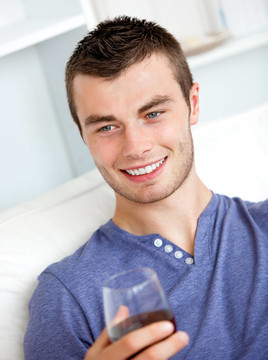 帥氣的年輕男子捧著一杯酒坐在客廳客廳的沙發(fā)上