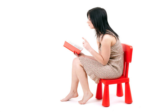 坐在紅色的；孩子的椅子年輕女子讀書