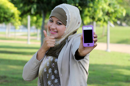年轻穆斯林妇女在头巾显示手机；拇指和文字空间