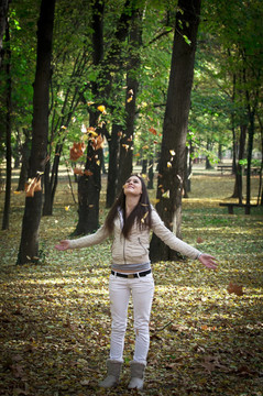 在美丽的森林里扔落叶的少女