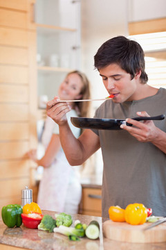 一個男人在廚房做飯，而他的女朋友正在廚房洗碗