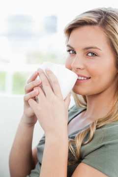 一個(gè)微笑的女人在她面前用一個(gè)杯子對(duì)著嘴唇。