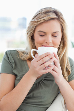 一個(gè)女人拿著一個(gè)杯子到她的鼻子；聞著她面前的杯子的味道。