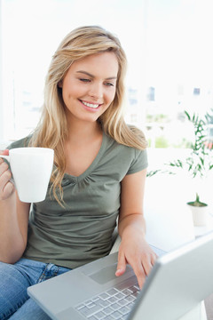 一個(gè)女人微笑著，一邊拿著筆記本一邊拿著一個(gè)杯子。