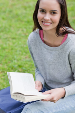 年輕快樂的女孩在公共花園看書，看著相機