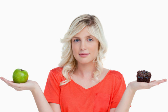 年輕的女人抱著一個巧克力松餅和她手中的青蘋果