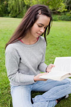 年輕的安靜女孩坐在草地上看書