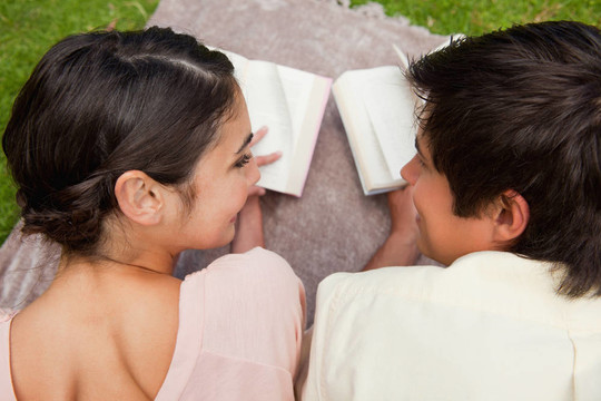一個男人和一個女人在看書的時候，看著他們趴在草地上的毯子上