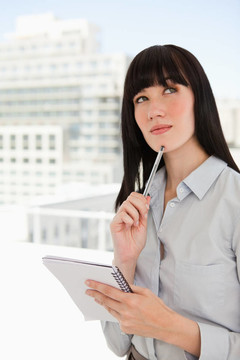 一個(gè)女人在辦公室里拿著一個(gè)記事本和一支筆放在下巴上，她想