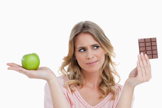 年轻女子拿着一个绿色的苹果看着巧克力棒