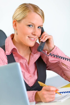 微笑的现代商务女性坐在办公桌前，用电话交谈
