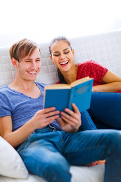 微笑的年輕夫婦坐在沙發(fā)上看書